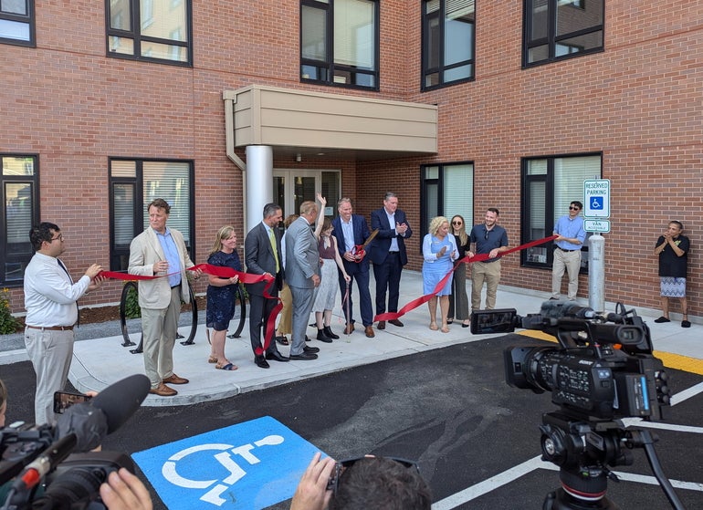 A gathering of people cutting a ceremonial ribbon in front of an apartment building