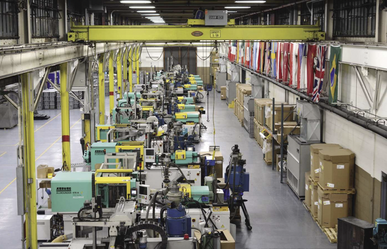 Inside a factory with yellow beams, green, yellow, and white machines, and flags lining the upper right hand wall.