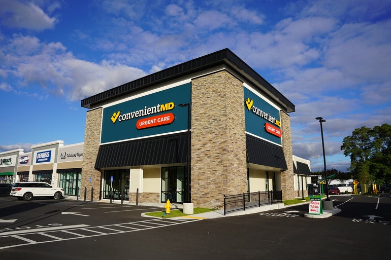 The outside of a  ConvenientMD location at the end corner of a strip mall, sitting behind a parking lot