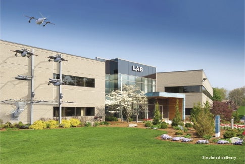 A large building with a sign reading "LAB" over the entrance sits behind a green lawn with trees and shrubs