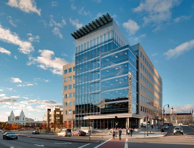 A tall glass building sits on a street corner with Worcester's Union Station in the background.