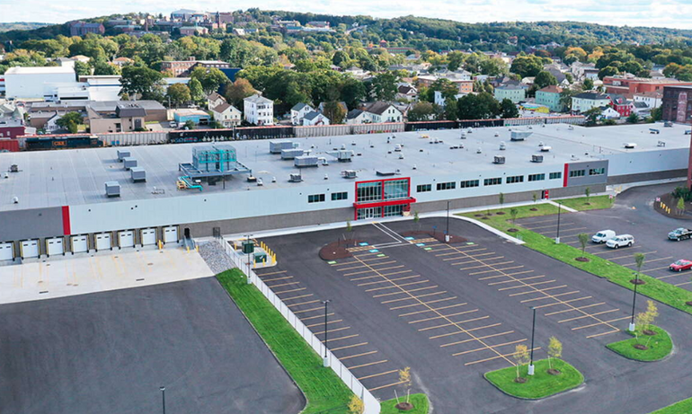 A large manufacturing building with residential and industrial cityscape behind it