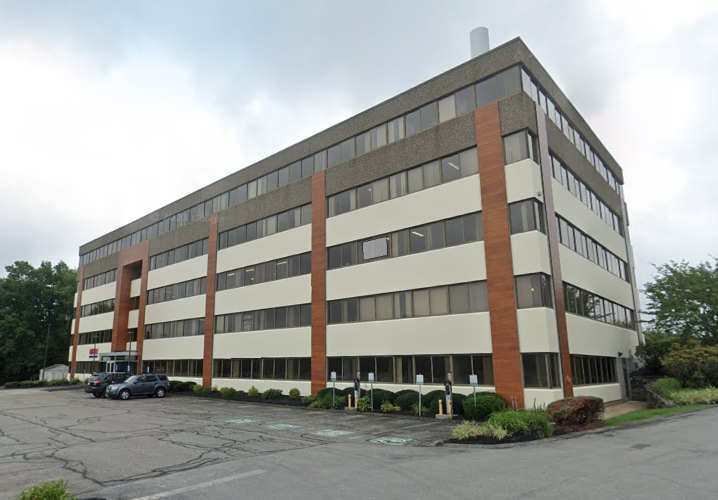 A building with black, tan, and brick siding sits in behind a parking lot.