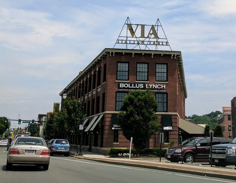 A three-story brick building with cars driving past on the left