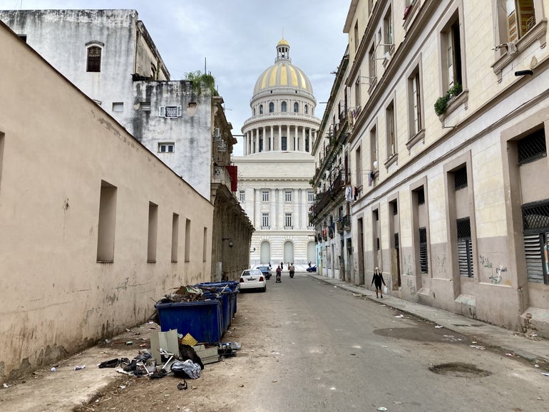 A large government building with a rotunda sits behind a mostly empty street with garbage piled up on one side