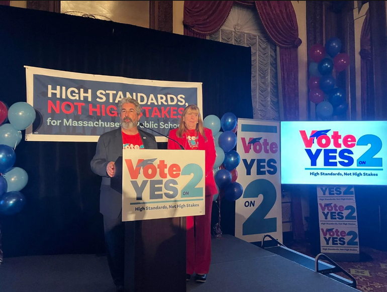 A man speaks at a podium while a woman stands besides him