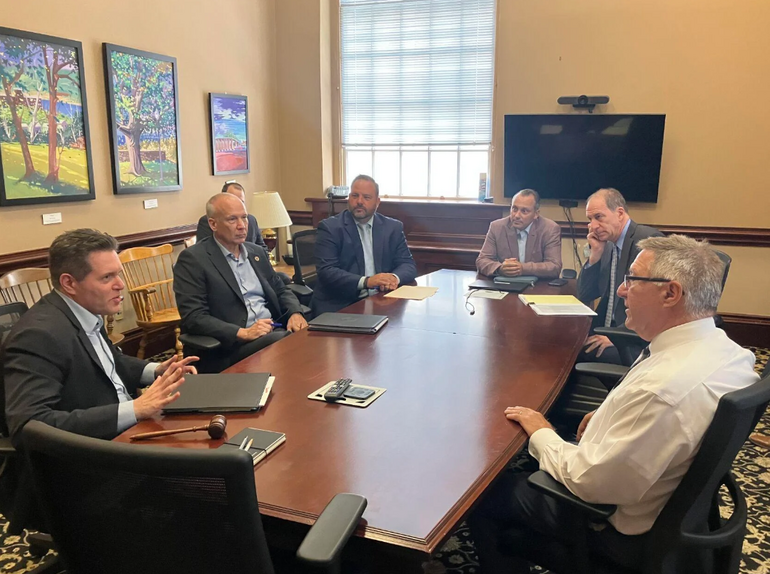 A group on men in suits talk at a conference table 
