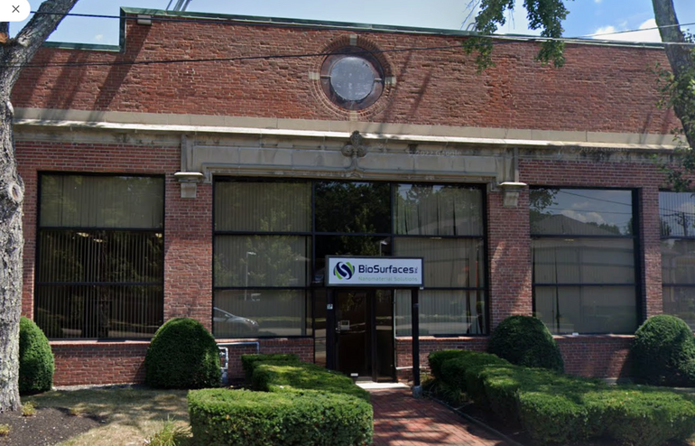 A brick building with trees in front sits behind a sidewalk.