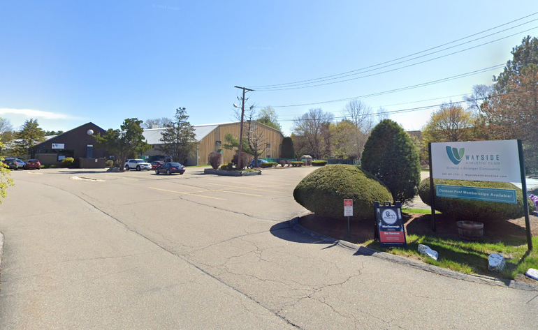 A parking lot and sign for a business sit in front of a one-story building 