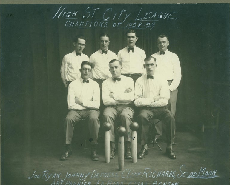 A photo from 1929 showing a candlepin bowling team, dressed in dress shirts with bowties and sitting in front of three pins with ball balancing on top.