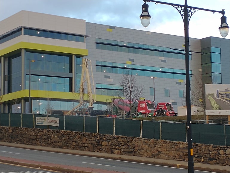 Concrete trucks pour concrete into the inside of a building behind construction fencing