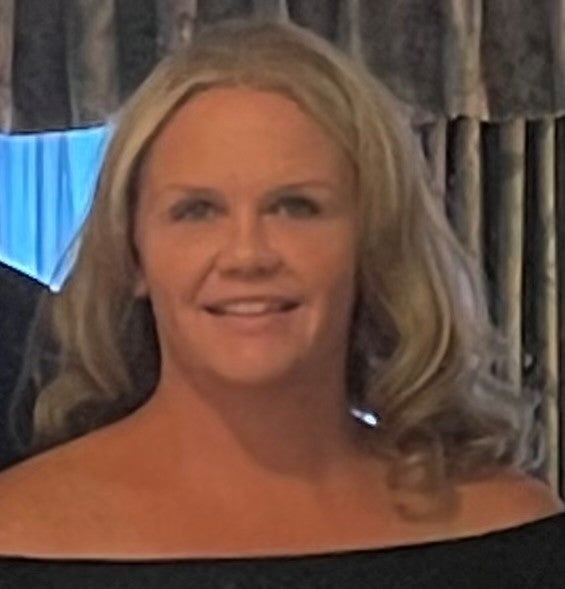 A woman with blonde hair wears a black off-the-shoulder top.