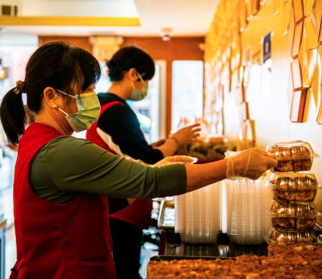 A woman with dark hair in a ponytail wears a red uniform stacking clear containers of desserts.