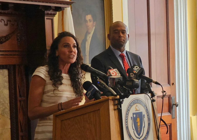 A woman speaks at a podium with a man standing alongside her