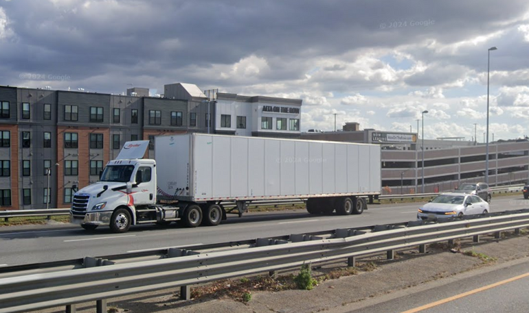 A white 18-wheeler drives down a highway