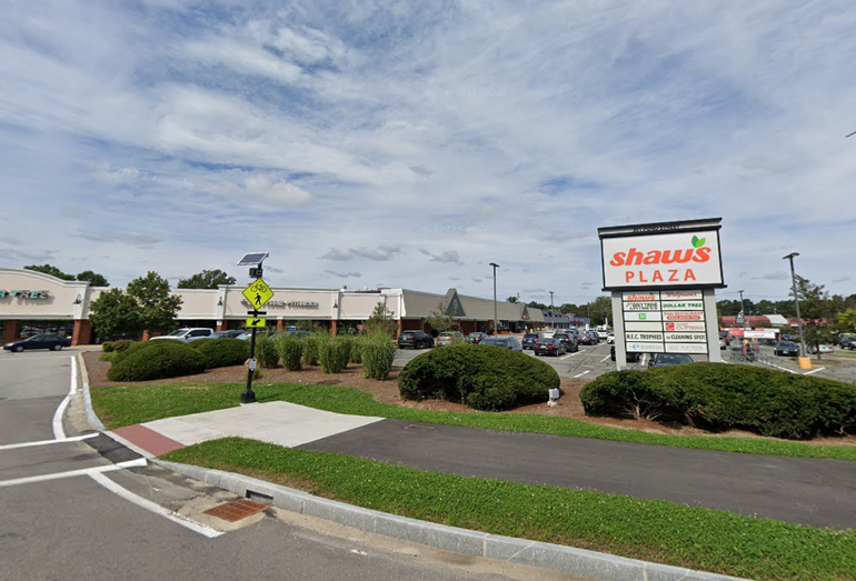 Entrance to a shopping plaza with a sign advertising its stores
