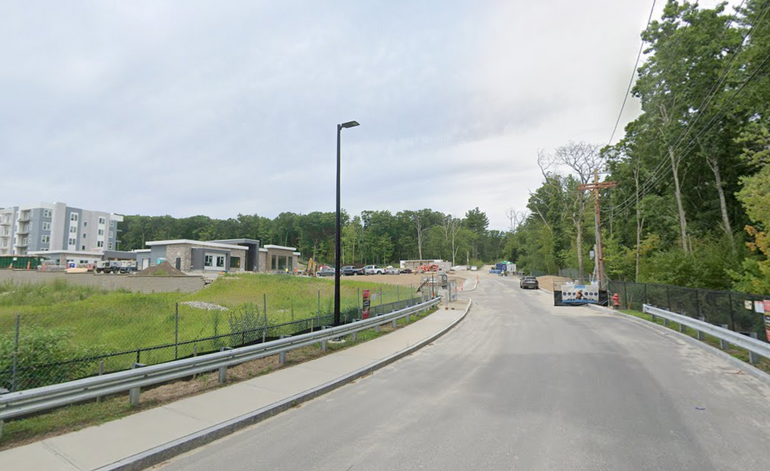 A road with a new apartment building to the left and construction vehicles and equipment to the right