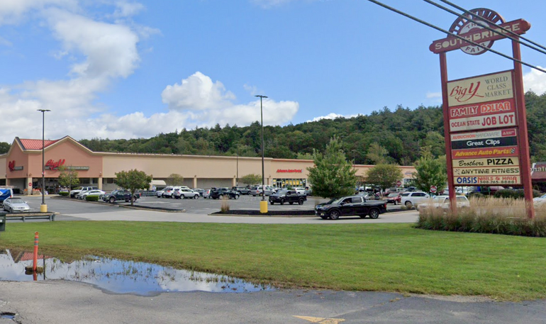 A shopping plaza with grass and puddle in front of