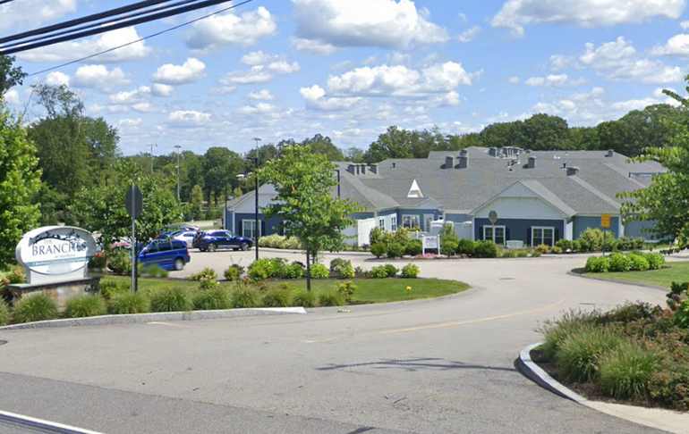 A one-story senior living building seen from the road, with a driveway and parking lot in between