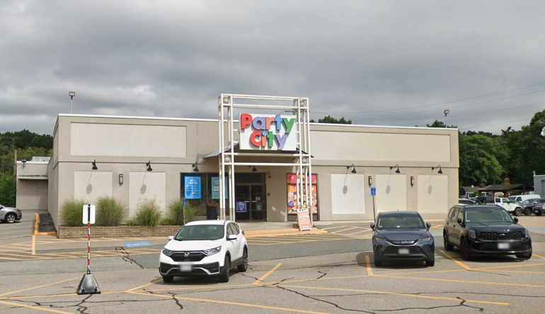 A one-story retail building with a grey stucco exterior and cars parked in front