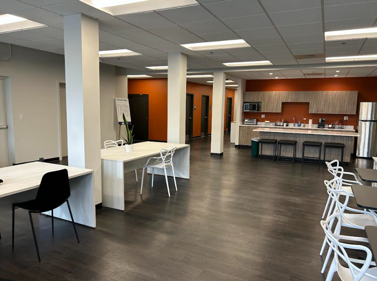 Inside a room with a kitchen at the back, white columns, tables and chairs.