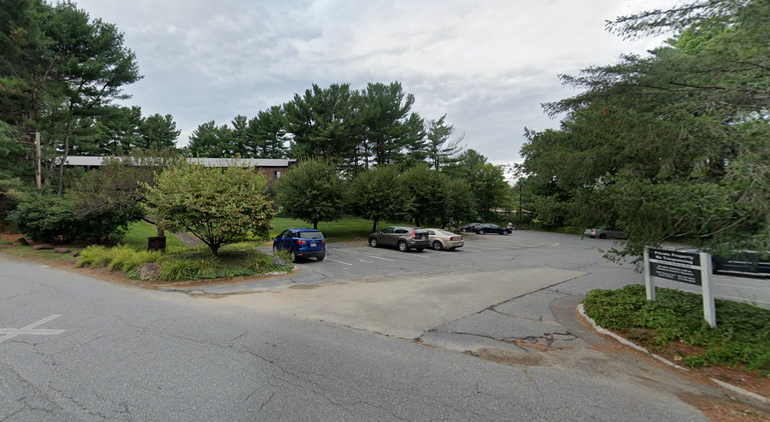 Parking lot with a small apartment building behind obscured by trees