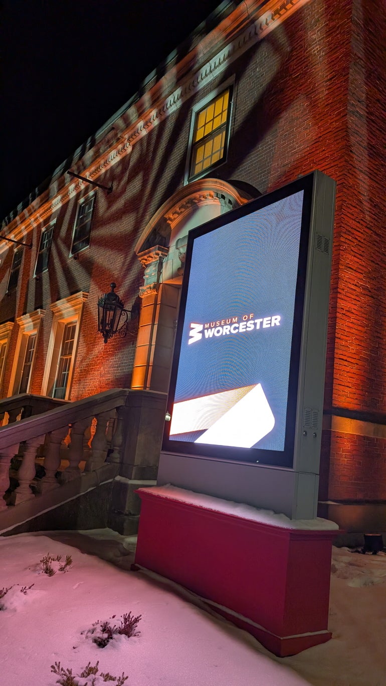 Outside a brick museum lit by patterned lights with a digital sign in front of it reading "Museum of Worcester"