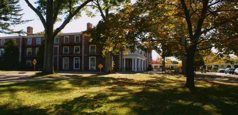 A brick hospital building sits behind a grassy field with trees.