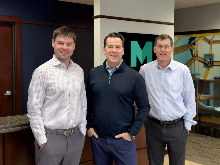 Three men in business attire pose for a photo in an office