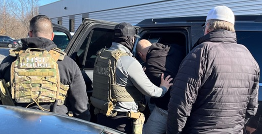 Two members of law enforcement escort an individual into a black van.