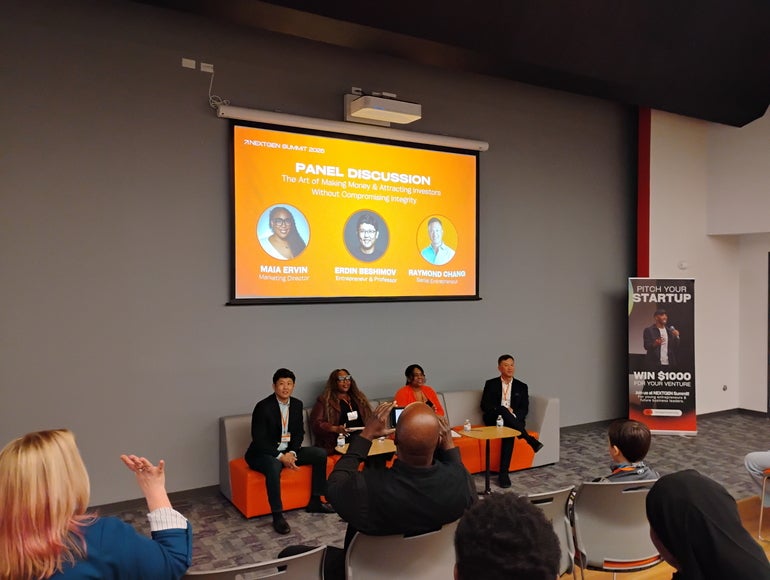 A panel discussion happening in an auditorium, with four speakers sitting in front of an audience