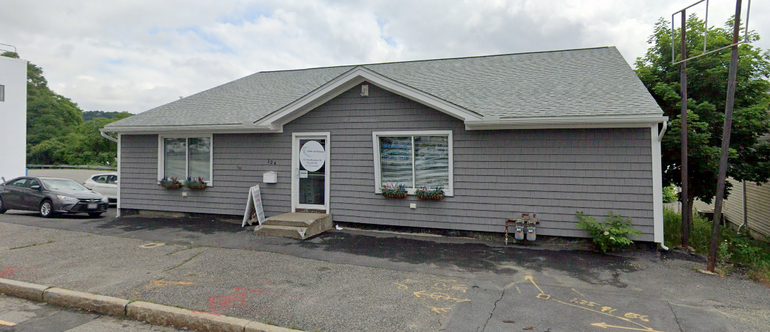 A house-like building with light blue siding sits behind a sidewalk with some spray paint on it.