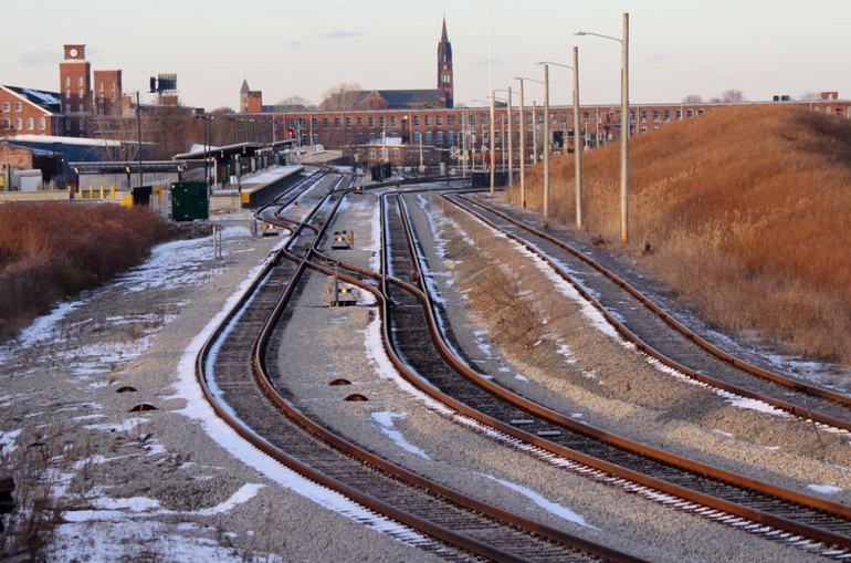 Railroad tracks with a light dusting of snow on them lead up to a city scape.