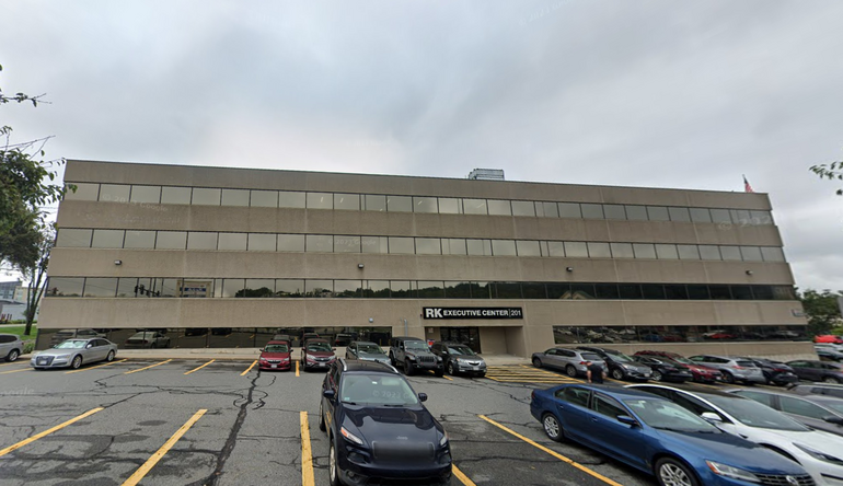 a four-story grey office building with a parking lot in front