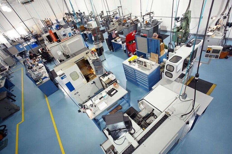 Inside a factory with white walls, a light blue floor, and machines colored white, blue, and green throughout the space