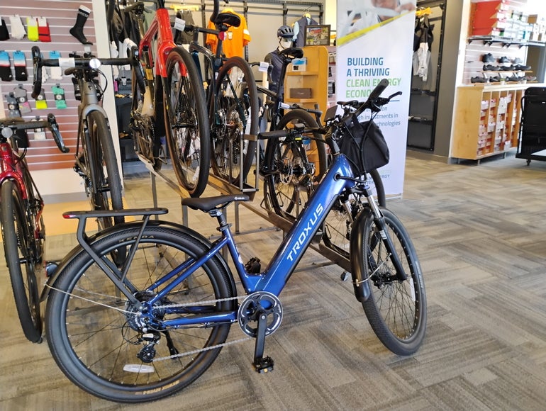 A blue e-bike sits on a bike shop floor I front of a rack of other bikes