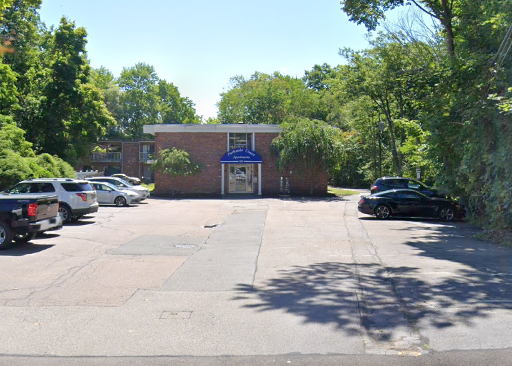 A two-story brick apartment building sits behind a small parking lot