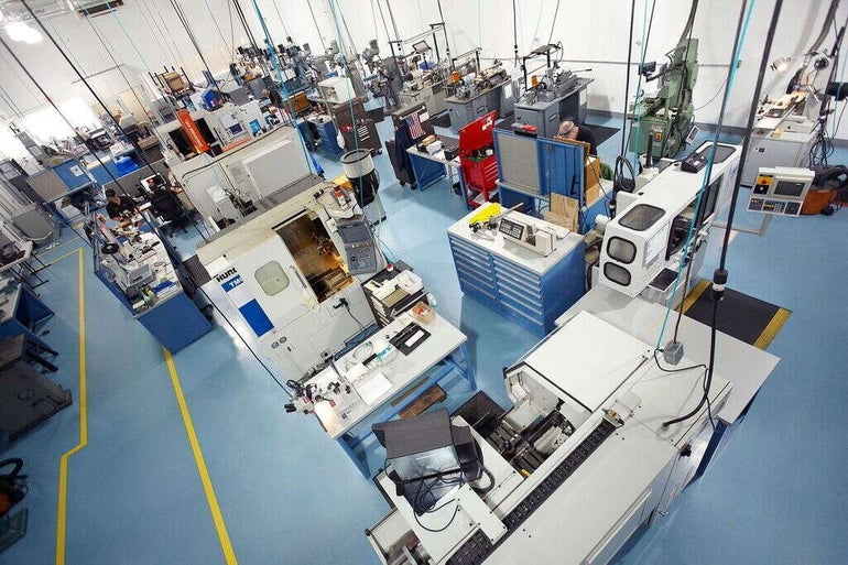 Inside a factory with white walls, a light blue floor, and machines colored white, blue, and green throughout the space