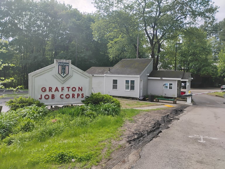 The entrance to a Job Corps center, with a sign to the left and a guard post and security gate to the right.