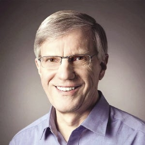 A  man with short grey hair wears glasses and a light purple button down.