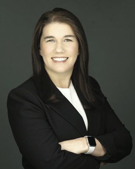A woman with dark hair wears a black blazer, a white top, and an Apple watch.