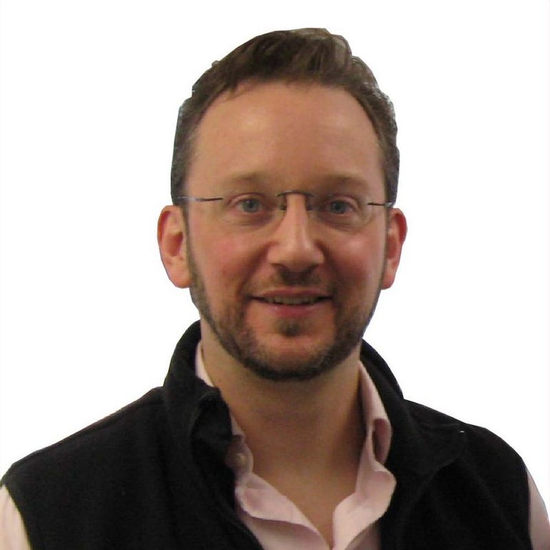 Headshot of man with glasses in a vest with salmon dress shirt underneath