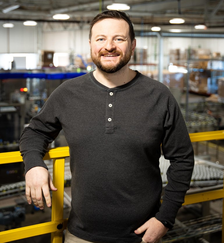 A man stands above a manufacturing floor, wearing a dark sweater.