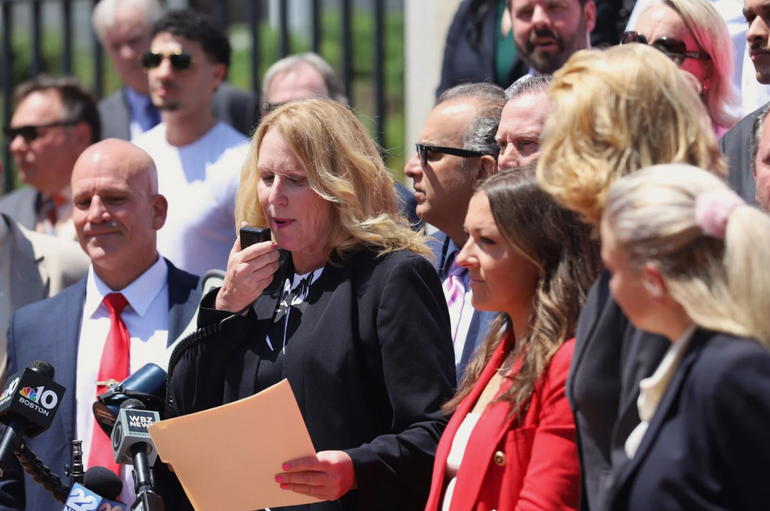 Woman speaks into megaphone microphone surrounded by a crowd of people in business attire. 