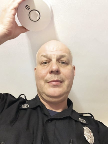 A man wearing a black uniform holds a fire alarm to a ceiling.