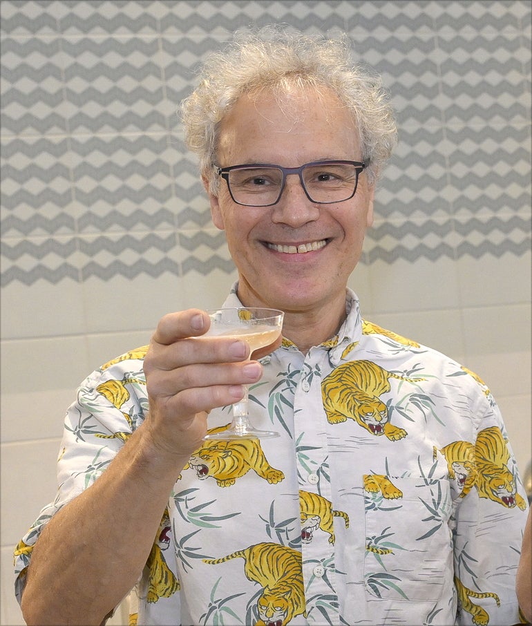 Man in dress shirt with tigers and leafs on it smiles while holding  a martini glass