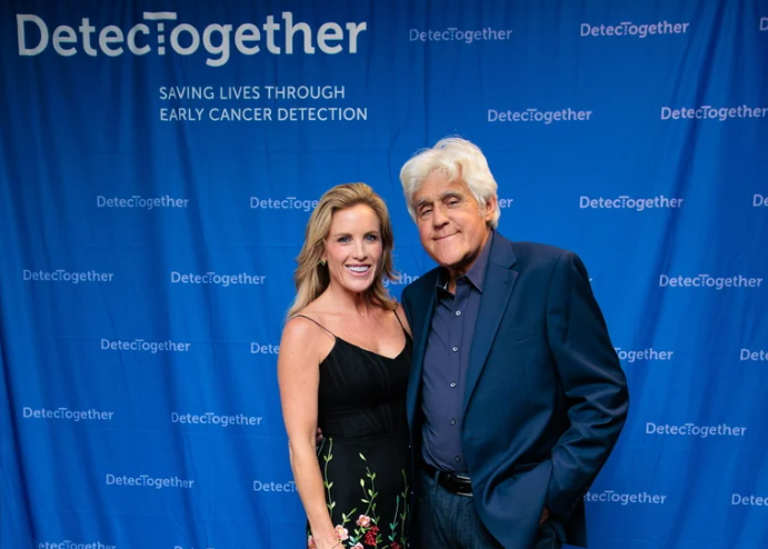 A man in a suit and a woman in a dress pose in front of a blue background