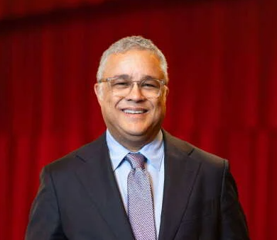 Man stands in suit in front of red curtain