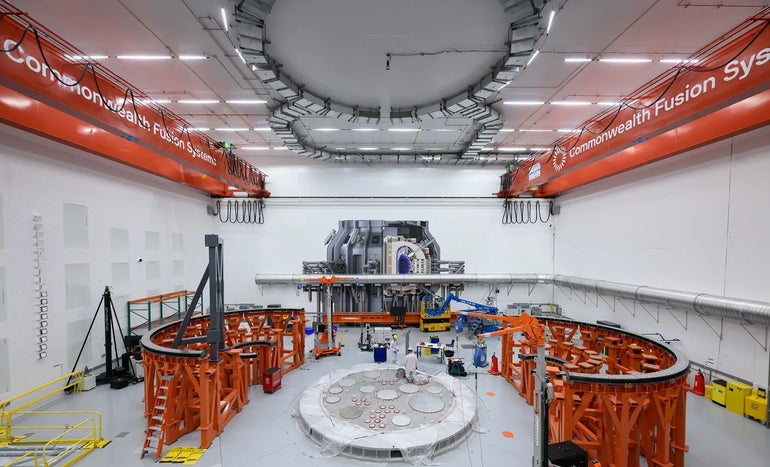 A large white room with orange machinery and workers in the middle