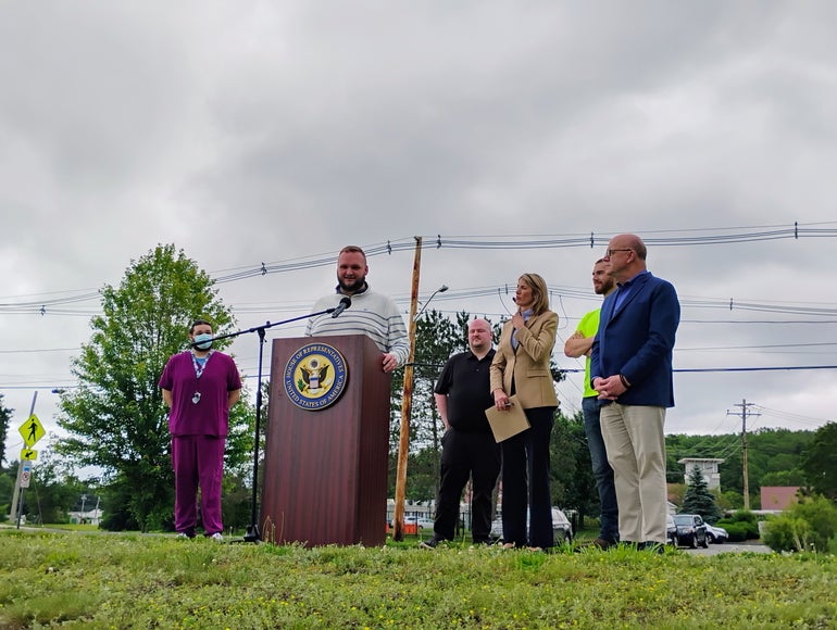 A man speaks at a podium as a group of people stand behind him